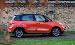 Pomarańczowy fiat 500xl z czarnym dachem stoi na tle ceglanej ściany.