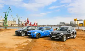 Trzy samochody BMW X: czarny, niebieski i kolejny czarny, stoją na placu budowy z dźwigami w tle.