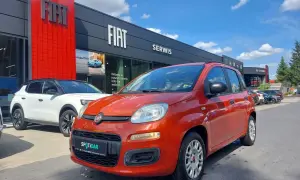 Pomarańczowy fiat panda używany z salonu czeka na nowego właściciela. Obok biały SUV.