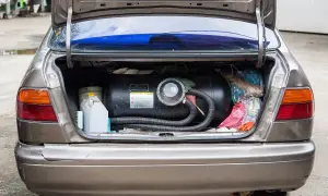 Bagażnik samochodu z zamontowanym zbiornikiem na gaz płynny LPG. Obok kanister i torby z zakupami.