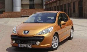 Pomarańczowy Peugeot 207 SW 1.4 benzyna zaparkowany na brukowanym placu przed ceglanym budynkiem.