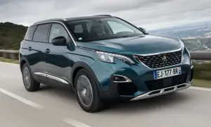 Peugeot 5008 wady i zalety: zielony SUV jedzie po krętej drodze z widokiem na góry.
