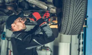 Mechanik w rękawicach dokręca sworzeń zwrotnicy w podwoziu samochodu.