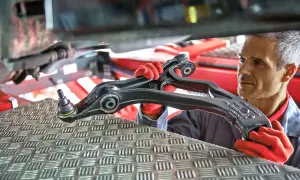 Mechanik w czerwonych rękawiczkach prezentuje nowy element zawieszenia samochodu, gotowy do montażu.