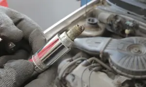 Ręka w rękawicy trzyma świecę zapłonową, potencjalną przyczynę błędu DTC P0301 w Volvo.