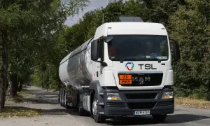 Biały cysterna z logo TSL jedzie drogą wśród drzew. To ważny element branży TSL, transportującej towary.