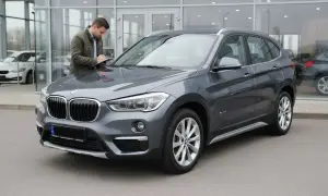 Szary BMW X1 F48, mężczyzna sprawdza dokumenty przy samochodzie. Czy to początek listy potencjalnych wad?