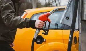 Tankowanie żółtego auta. Dłoń trzymająca pistolet dystrybutora, gotowa do nalania paliwa. Gęstość oleju napędowego jest kluczowa dla sprawnego działania silnika.