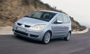 Srebrny Mitsubishi Colt VI pokonuje zakręt na krętej drodze, otoczony przez wzgórza.