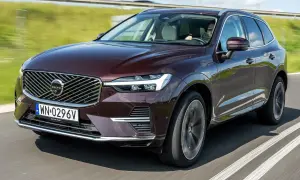 Elegancki, bordowy Volvo XC60 T5 w ruchu drogowym. Kierowca w okularach prowadzi SUV-a po asfaltowej drodze, otoczonej zielenią.