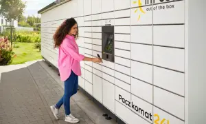 Kobieta z telefonem przy Paczkomacie InPost. Szybka wysyłka paczek za granicę jest teraz prosta.
