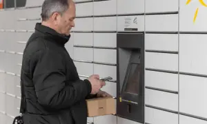 Mężczyzna z paczką i telefonem przy paczkomacie tymczasowym.