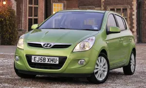 Zielony Hyundai i20 z włączonymi światłami przeciwmgielnymi przednimi, zaparkowany przed ceglanym budynkiem.
