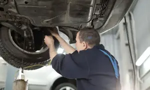 Mechanik wymienia płyn hamulcowy w Golfie 4. Pod samochodem widać podnośnik i narzędzia.