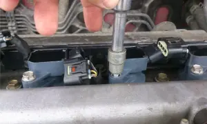 Dłoń z kluczem nasadowym dokręca cewkę zapłonową. Widać kilka cewek, złącza elektryczne i śruby mocujące. To część naprawy silnika, być może związana z kodem błędu p0300.
