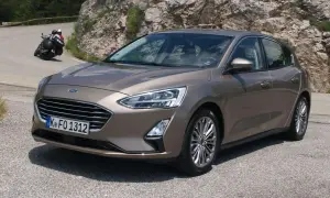 Brązowy Ford Focus 2017 na krętej drodze, z motocyklistą w tle.