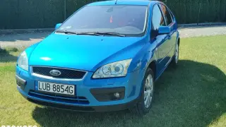 Błękitny Ford Focus MK2 1.6 benzyna zaparkowany na trawie.