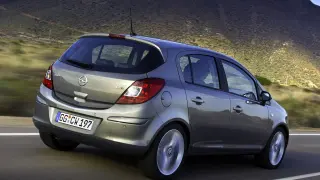 Szary Opel Corsa D 1.2 benzyna w ruchu, z widokiem na tył i bok, na tle górskiego krajobrazu.