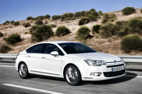 Biały Citroen C5 z hydropneumatycznym zawieszeniem jedzie po drodze. Zastanawiasz się nad citroen c5 zawieszenie hydropneumatyczne koszt naprawy?
