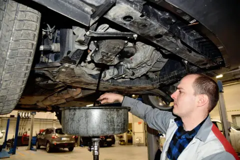 Mechanik spuszcza stary olej z silnika, przypominając o regularnej wymianie oleju dla sprawnego działania auta.
