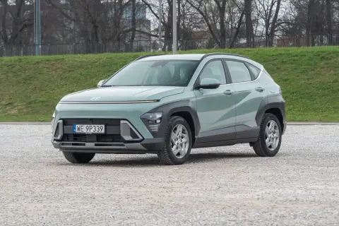 Nowy Hyundai Kona 1.6 benzyna w pastelowym kolorze, zaparkowany na żwirowym placu, gotowy na miejskie przygody.