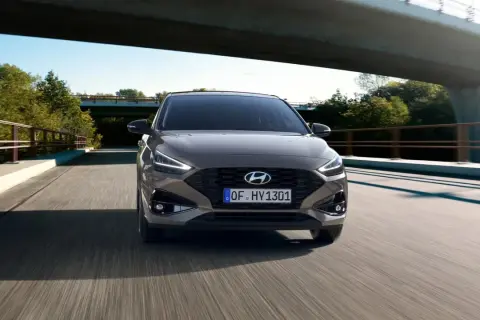 Nowy Hyundai i30 2023 w kolorze brązowym jedzie po moście wśród zieleni.