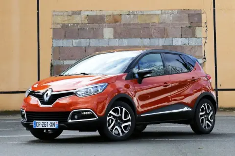 Pomarańczowy Renault Captur 2016 z czarnym dachem stoi przed ceglaną ścianą.
