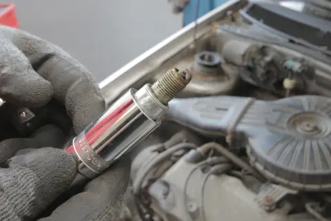 Ręka w rękawicy trzyma świecę zapłonową, potencjalną przyczynę błędu DTC P0301 w Volvo.