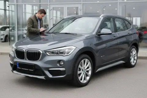 Szary BMW X1 F48, mężczyzna sprawdza dokumenty przy samochodzie. Czy to początek listy potencjalnych wad?
