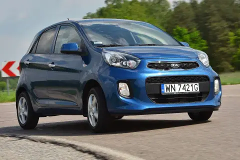 Niebieski Kia Picanto 2012 na drodze, z zielonymi drzewami w tle.