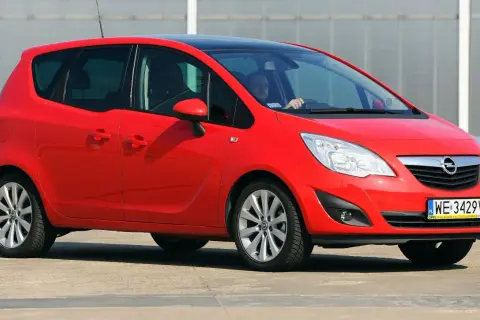 Czerwony Opel Meriva 1.6 benzyna z czarnym dachem, zaparkowany na zewnątrz. Kierowca w okularach siedzi za kierownicą.