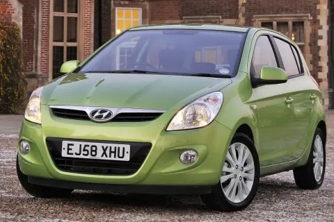 Zielony Hyundai i20 z włączonymi światłami przeciwmgielnymi przednimi, zaparkowany przed ceglanym budynkiem.