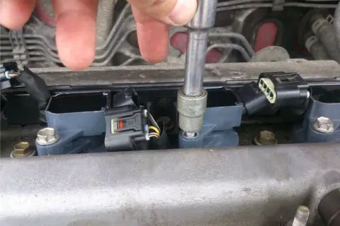 Dłoń z kluczem nasadowym dokręca cewkę zapłonową. Widać kilka cewek, złącza elektryczne i śruby mocujące. To część naprawy silnika, być może związana z kodem błędu p0300.