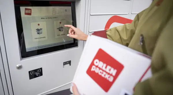 Kobieta z paczką ORLEN Paczka dotyka ekranu automatu paczkowego, wybierając opcję nadania przesyłki.