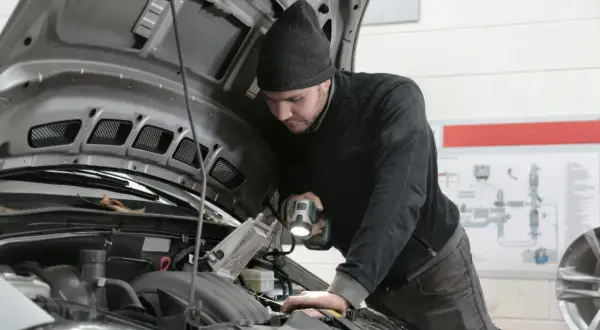 Mechanik z latarką bada silnik Renault, szukając przyczyny błędu DTC P0380.