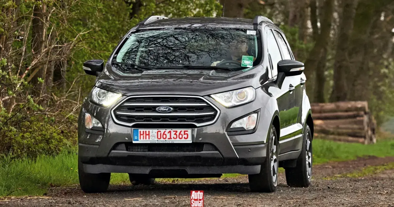 Szary Ford Ecosport na leśnej drodze. Kierowca w okularach za kierownicą.