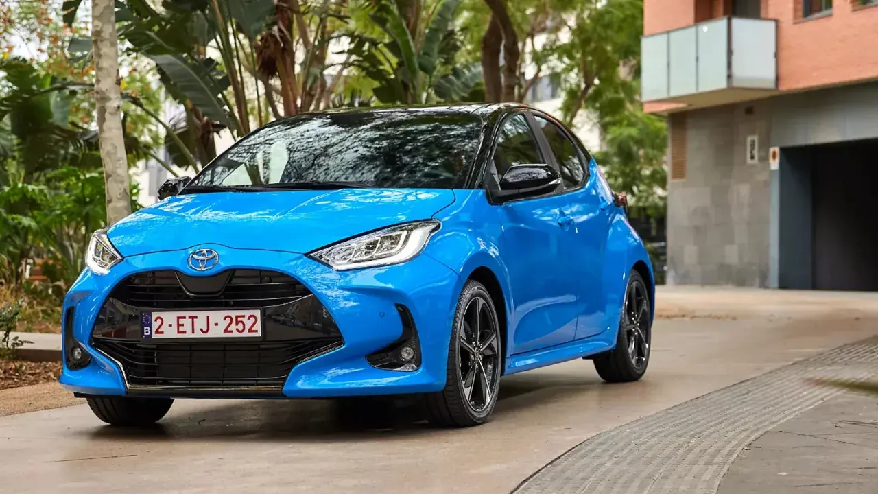 Błękitna Toyota Yaris 1.3 benzyna zaparkowana na tle zieleni i budynku. Zastanawiasz się, jaki olej do toyoty yaris 1.3 benzyna?