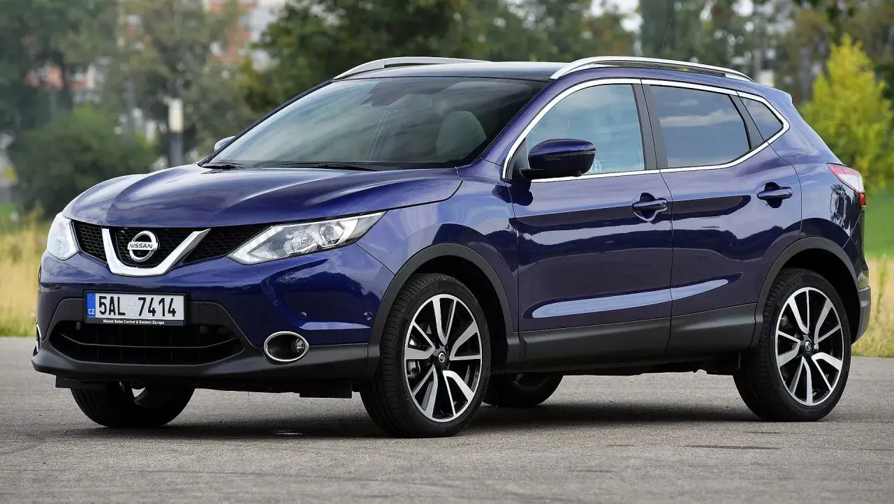 Granatowy Nissan Qashqai J11 z chromowanymi relingami dachowymi i felgami stoi na drodze.