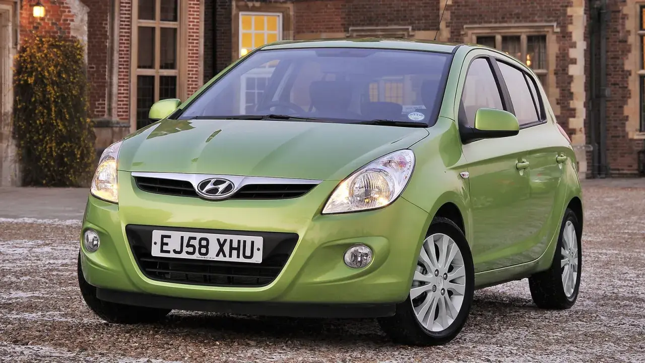 Zielony Hyundai i20 z włączonymi światłami przeciwmgielnymi przednimi, zaparkowany przed ceglanym budynkiem.