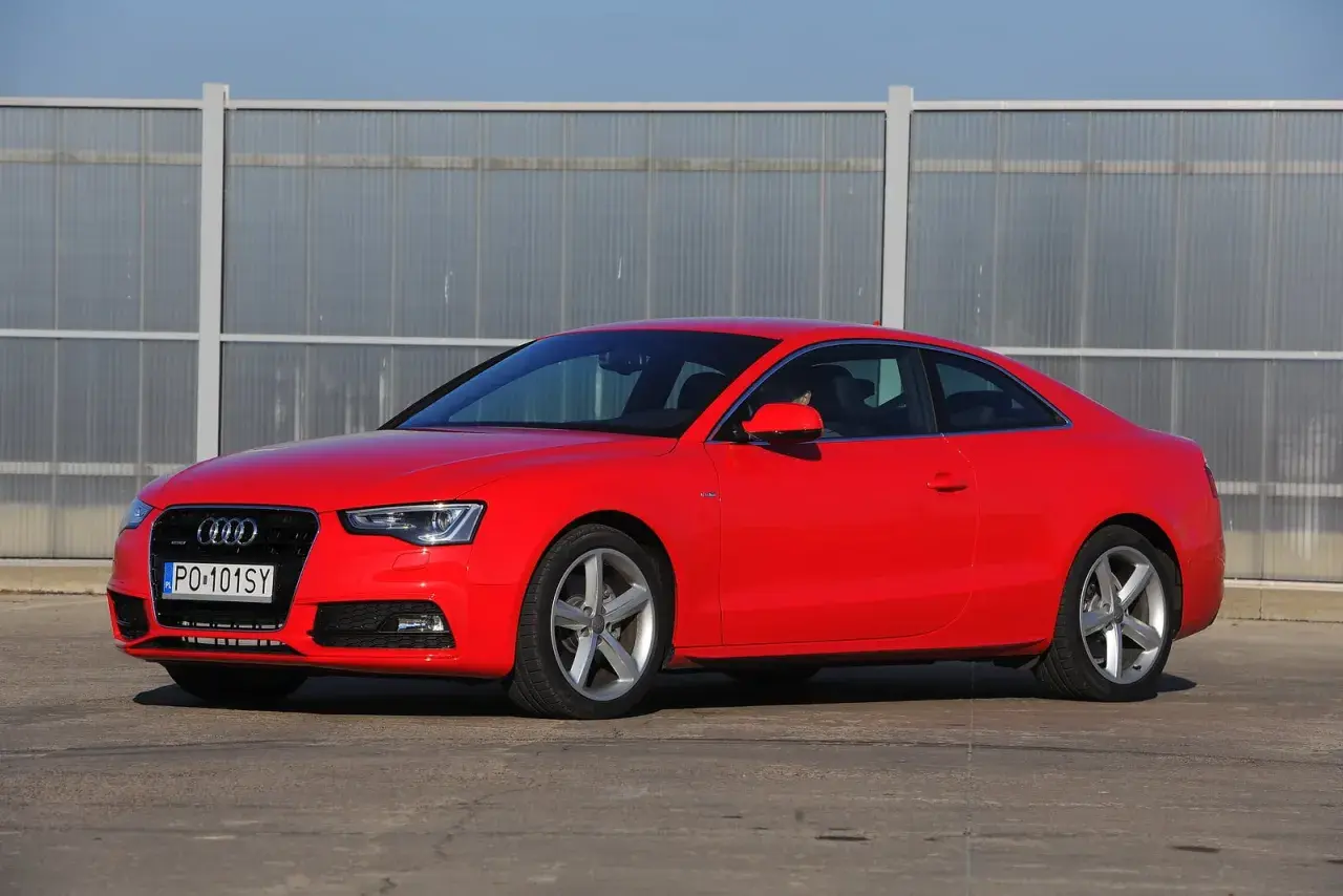 Czerwone Audi S5 z 2014 roku, sportowe coupe z elegancką linią, zaparkowane przed nowoczesnym budynkiem.