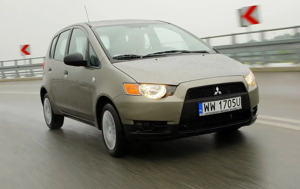 Złoty Mitsubishi Colt VI jedzie po mokrej drodze.