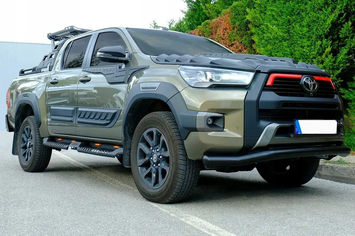 Zielony Toyota Hilux Invincible z czarnymi dodatkami, relingami dachowymi i terenowymi oponami. Gotowy na każdą przygodę.