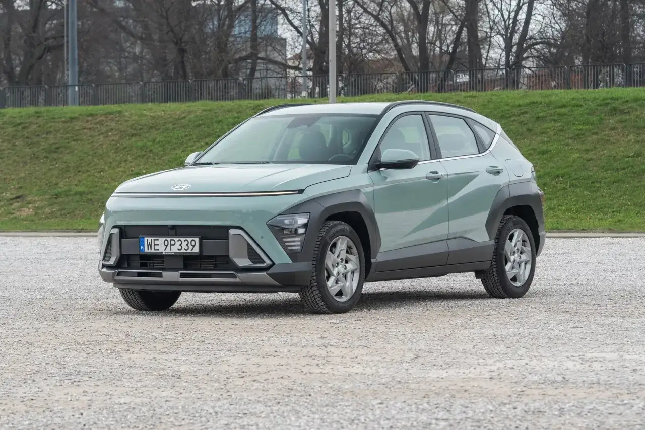 Nowy Hyundai Kona 1.6 benzyna w pastelowym kolorze, zaparkowany na żwirowym placu, gotowy na miejskie przygody.