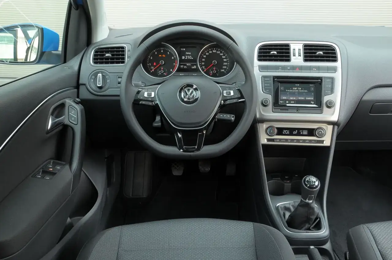 Wnętrze VW Polo 2010: kierownica, deska rozdzielcza z radiem i klimatyzacją, dźwignia zmiany biegów.