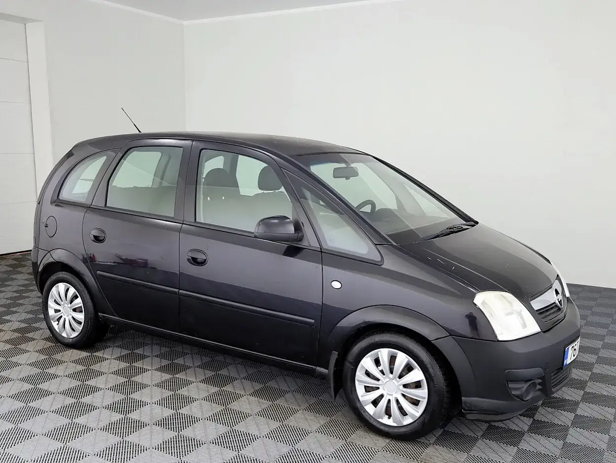 Ciemnoszary Opel Meriva na tle białej ściany. Widoczne felgi i opony, których rozmiar jest kluczowy dla tego modelu.