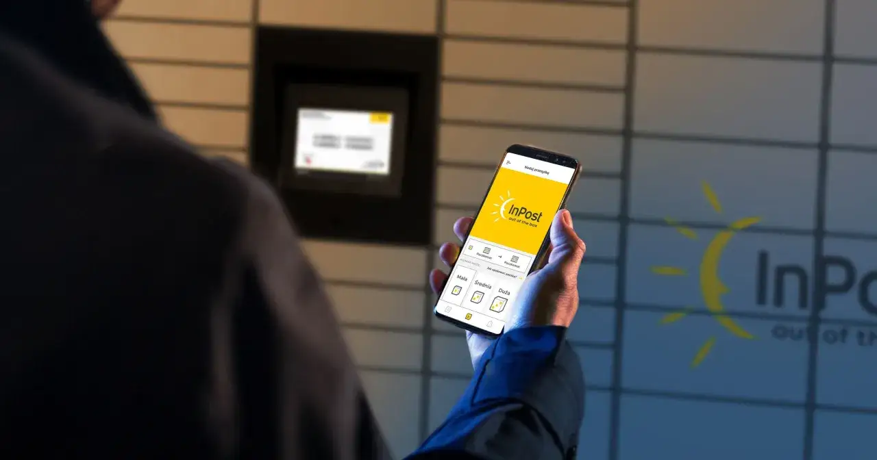 Mężczyzna trzyma smartfon z aplikacją InPost, obok znajduje się paczkomat.