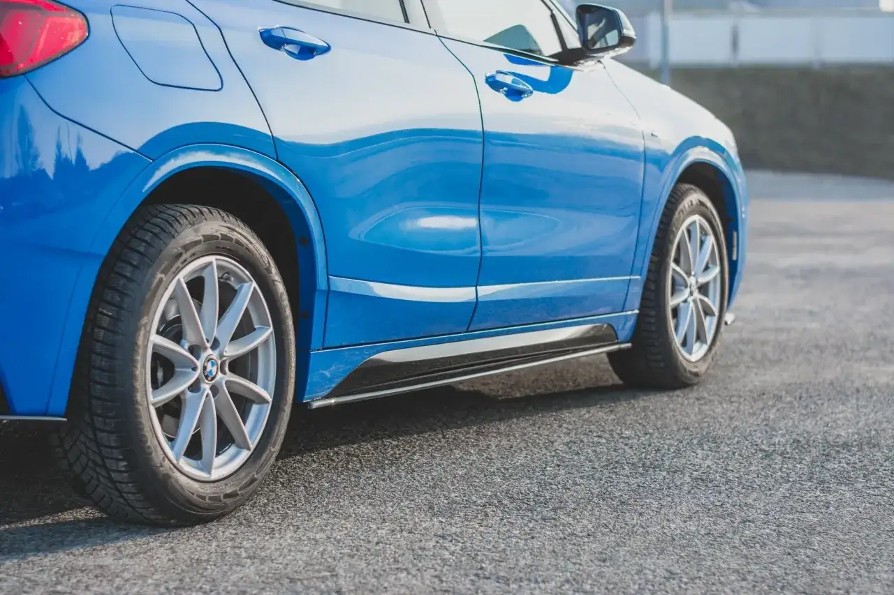 Błękitne BMW F39 z felgami i oponami zimowymi stoi na asfalcie.