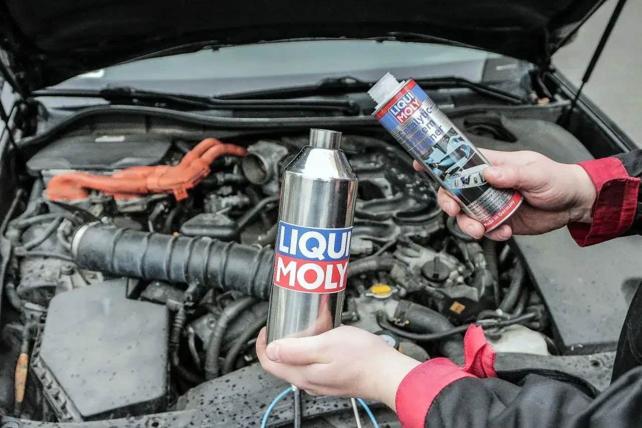 Dwie ręce trzymają preparaty Liqui Moly do czyszczenia układu wydechowego, w tym katalizatora w samochodzie.