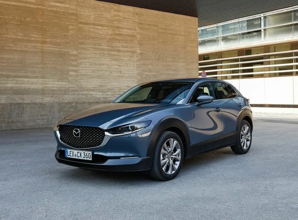 Szary Mazda CX-30 stoi przed nowoczesnym budynkiem. Choć auto ma wiele zalet, warto znać jego wady przed zakupem.