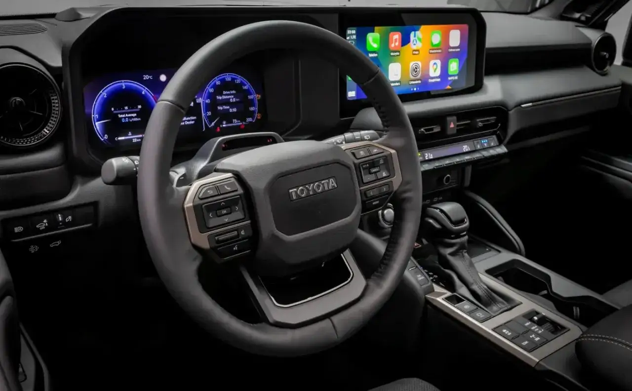 Wnętrze Toyota Land Cruiser 2020: kierownica z przyciskami, cyfrowe zegary i ekran multimedialny.